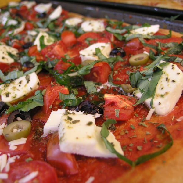 Close-up of a rectangular pizza with tomatoes, mozzarella, olives, and basil.
