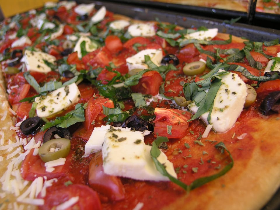 Close-up of a rectangular pizza with tomatoes, mozzarella, olives, and basil.