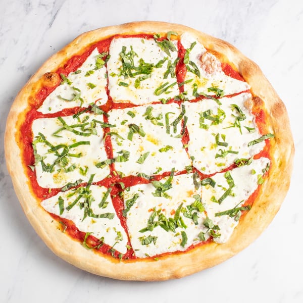 A freshly baked Margherita pizza, sliced into squares, with vibrant red sauce, white mozzarella, and green basil.