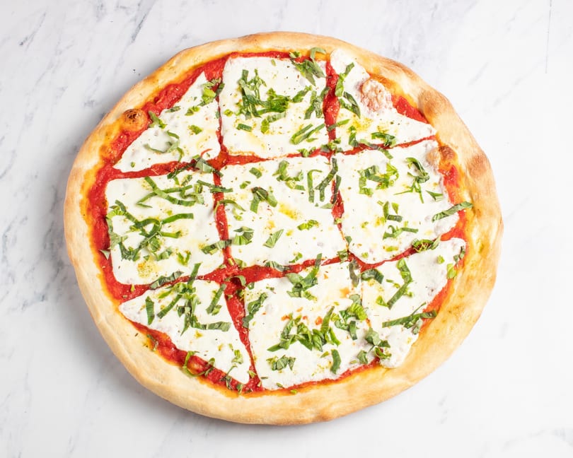 A freshly baked Margherita pizza, sliced into squares, with vibrant red sauce, white mozzarella, and green basil.