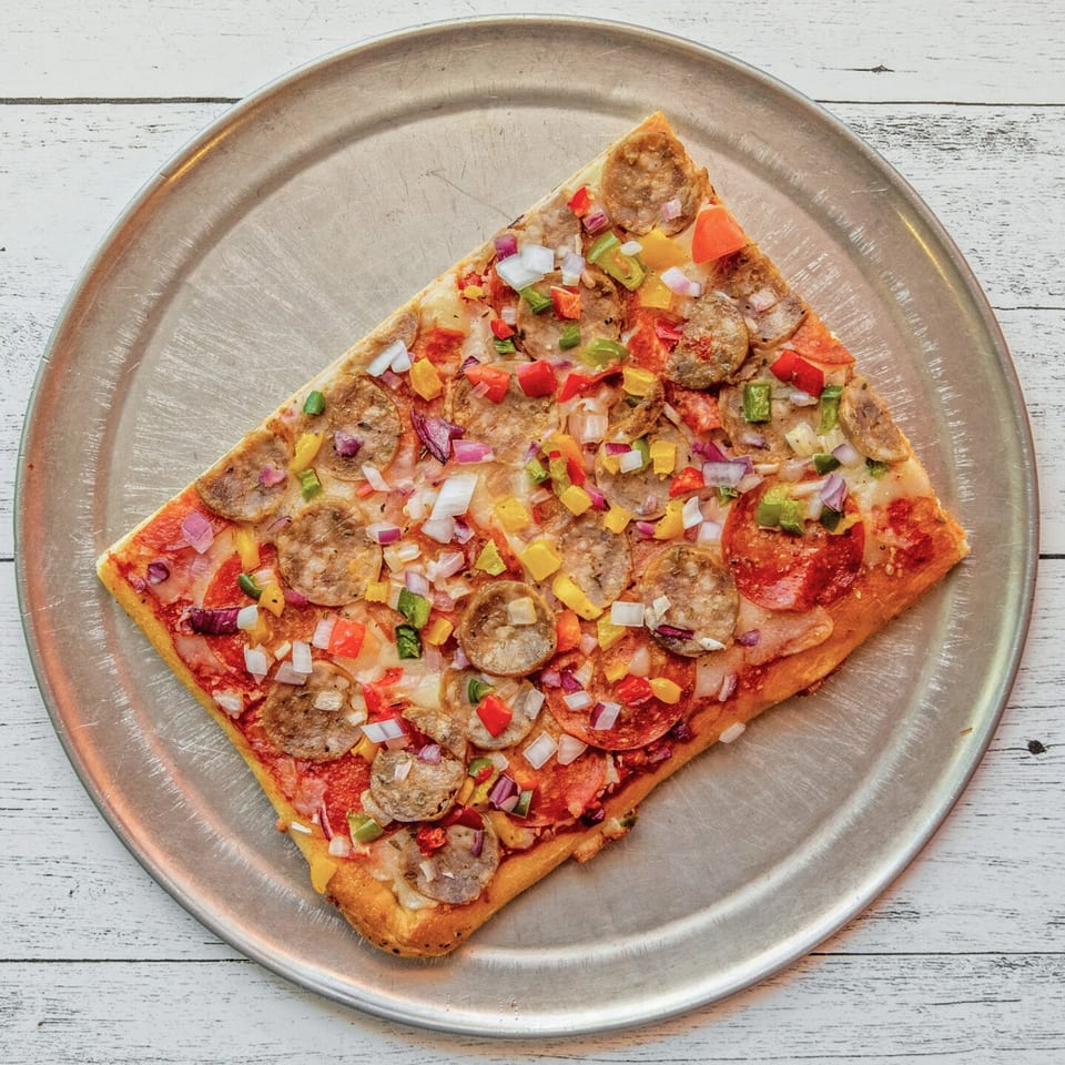 Rectangular pizza with pepperoni, sausage, and colorful diced vegetables on a metal pan.