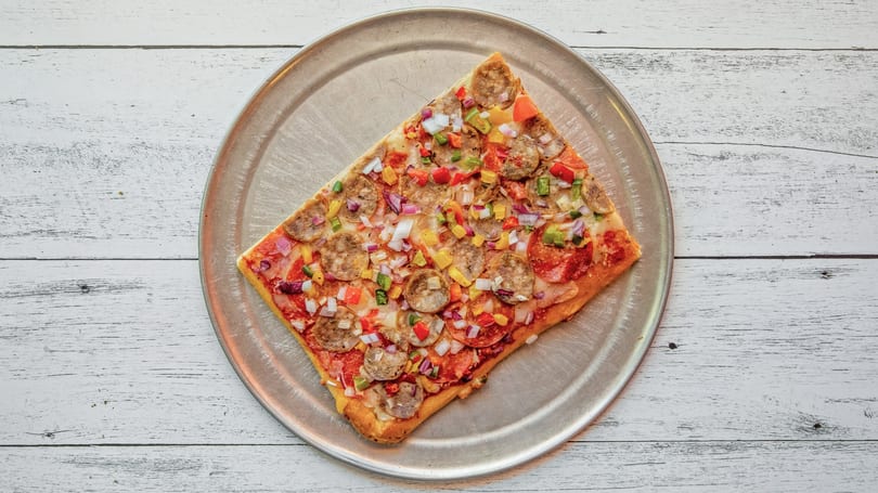 Rectangular pizza with pepperoni, sausage, and colorful diced vegetables on a metal pan.