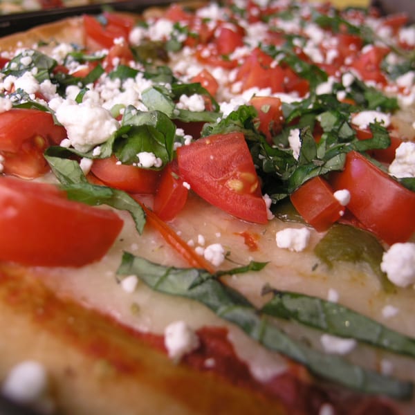 Close-up of a pizza slice topped with diced tomatoes, crumbled feta cheese, and fresh basil.