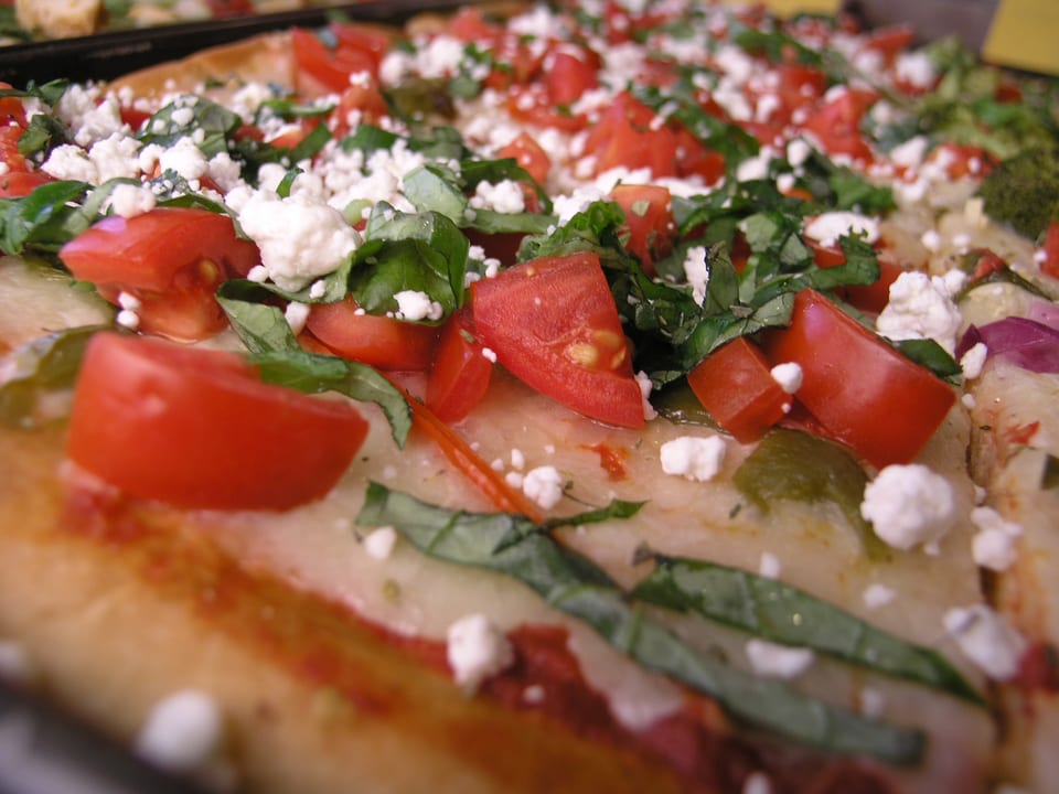 Close-up of a pizza slice topped with diced tomatoes, crumbled feta cheese, and fresh basil.