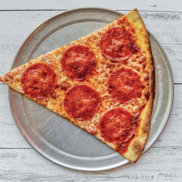 A single slice of pepperoni pizza on a metal tray, viewed from above on a white wooden table.